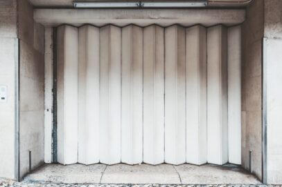 A garage accordion-folded gates Garage or entrance closed metal gates texture with white vertical fanfold lines of the door; front view of an accordion-folded painted door of a big gate on the street, common in Lisbon, Portugal