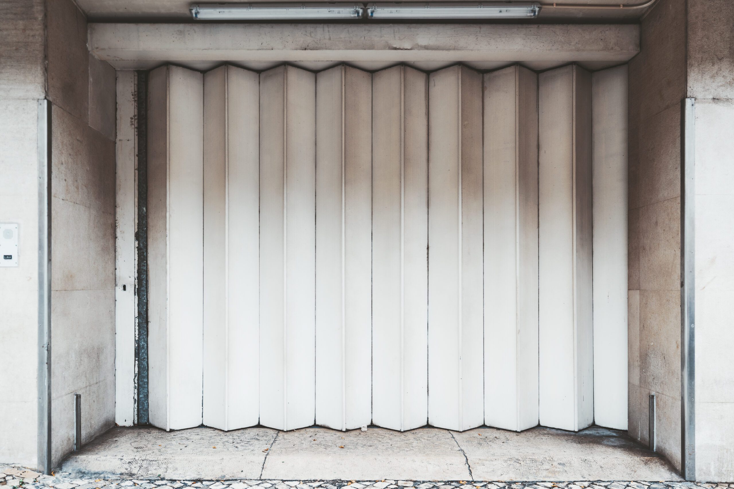 Building Removing Partition Walls 11 Garage or entrance closed metal gates texture with white vertical fanfold lines of the door; front view of an accordion-folded painted door of a big gate on the street, common in Lisbon, Portugal